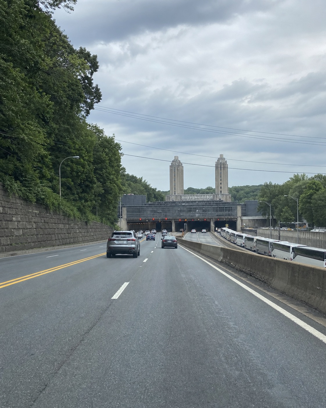 AI-generated tunnel-approach scene with a portal, towers and buses beyond a divider, inspired by the Lincoln Tunnel approach. Not a verified location, current map or real crash photograph.